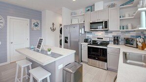 Une cuisine moderne avec des meubles blancs, des appareils en acier inoxydable et un îlot central doté de tabourets.