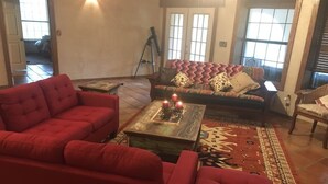 Ein Wohnzimmer mit einem roten Sofa, einem gemusterten Sofa und einem Couchtisch aus Holz mit Kerzen.