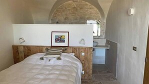 Een slaapkamer met een houten hoofdeinde, een bed met een gestreept kussen, een ingelijst schilderij aan de muur en een zichtbare badkamer door een boog.