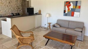 Een moderne woonruimte met een stenen muur, een kitchenette, een grijze bank, een houten stoel en een salontafel.