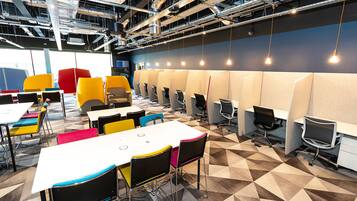 Un espace de bureau moderne doté d’un sol à motifs géométriques, de plusieurs tables et chaises, ainsi que d’une rangée de bureaux individuels séparés par des cloisons.