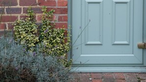 A light blue door with a brass handle, a brass doorbell, and a sign reading "The Coach House" on a brick wall.