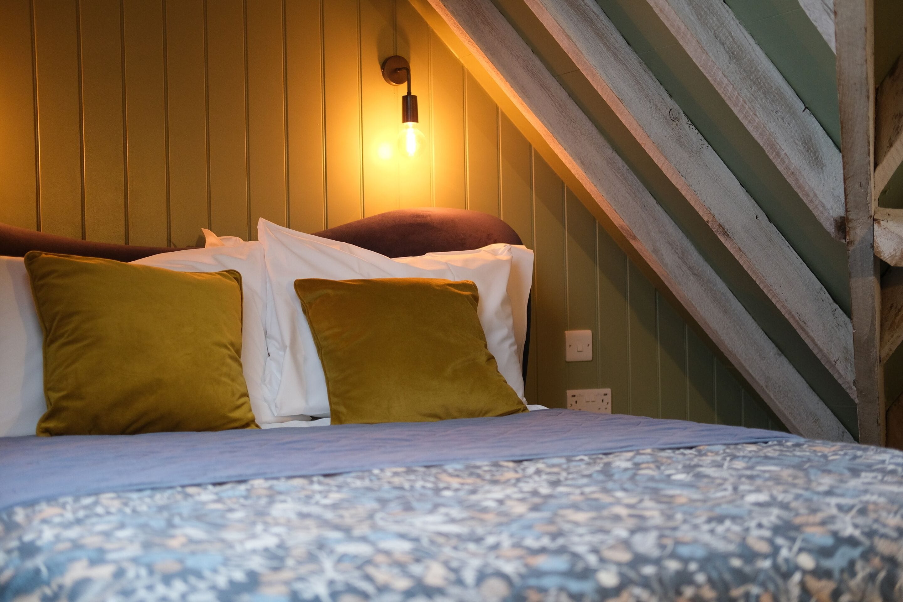 A bed with a patterned bedspread, two pillows, and a wall-mounted light fixture.
