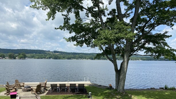 A lakeside deck with outdoor seating and a grill, overlooking a calm lake with distant hills. - Sunrise, Sunset, Relax, Repeat Lamoka Cove (Bradford)