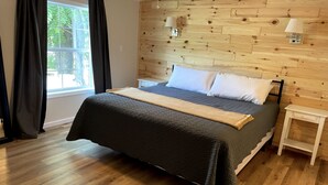 A neatly arranged bedroom with a wooden headboard, a large bed with a dark quilt, white pillows, and a bedside table with a lamp. - Sunrise, Sunset, Relax, Repeat Lamoka Cove (Bradford)