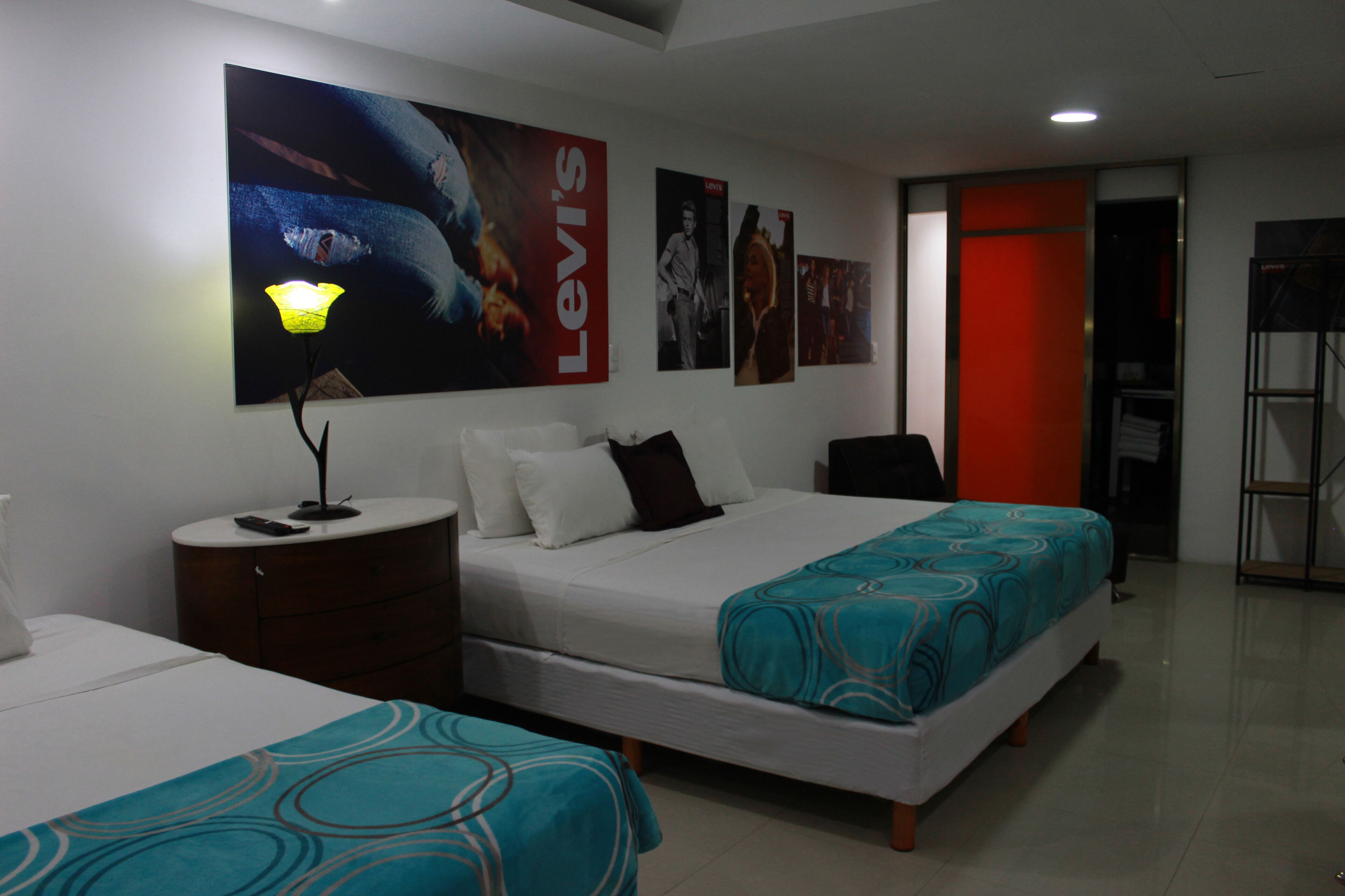 A hotel room with two beds, a nightstand, a lamp, and a large poster on the wall.