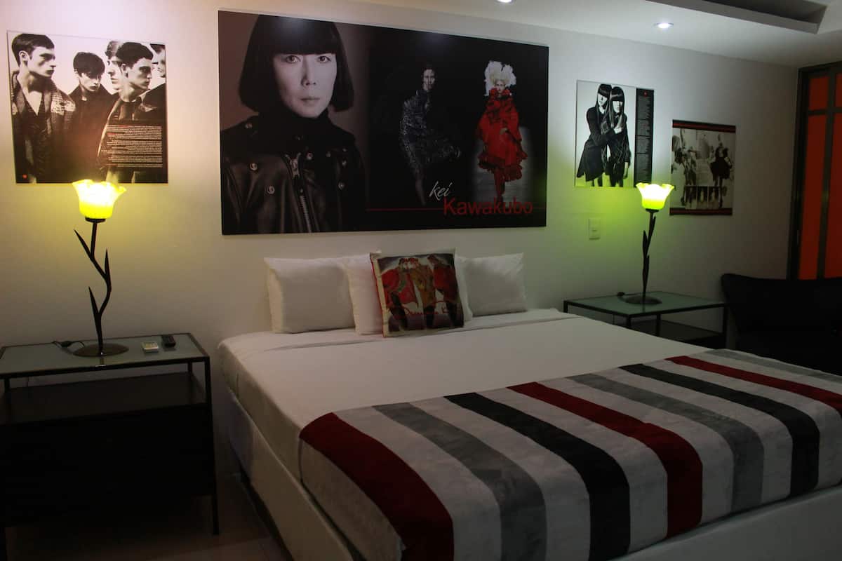 A hotel room with a large bed, two bedside tables, and wall art.