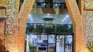 A building entrance with a stone archway, potted plants, and a paved walkway leading to an interior space with tables and chairs. - Essenzia de Cancun (Cancun)