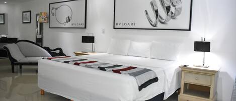 A modern hotel room with a large bed, a chair, a nightstand, and wall art.