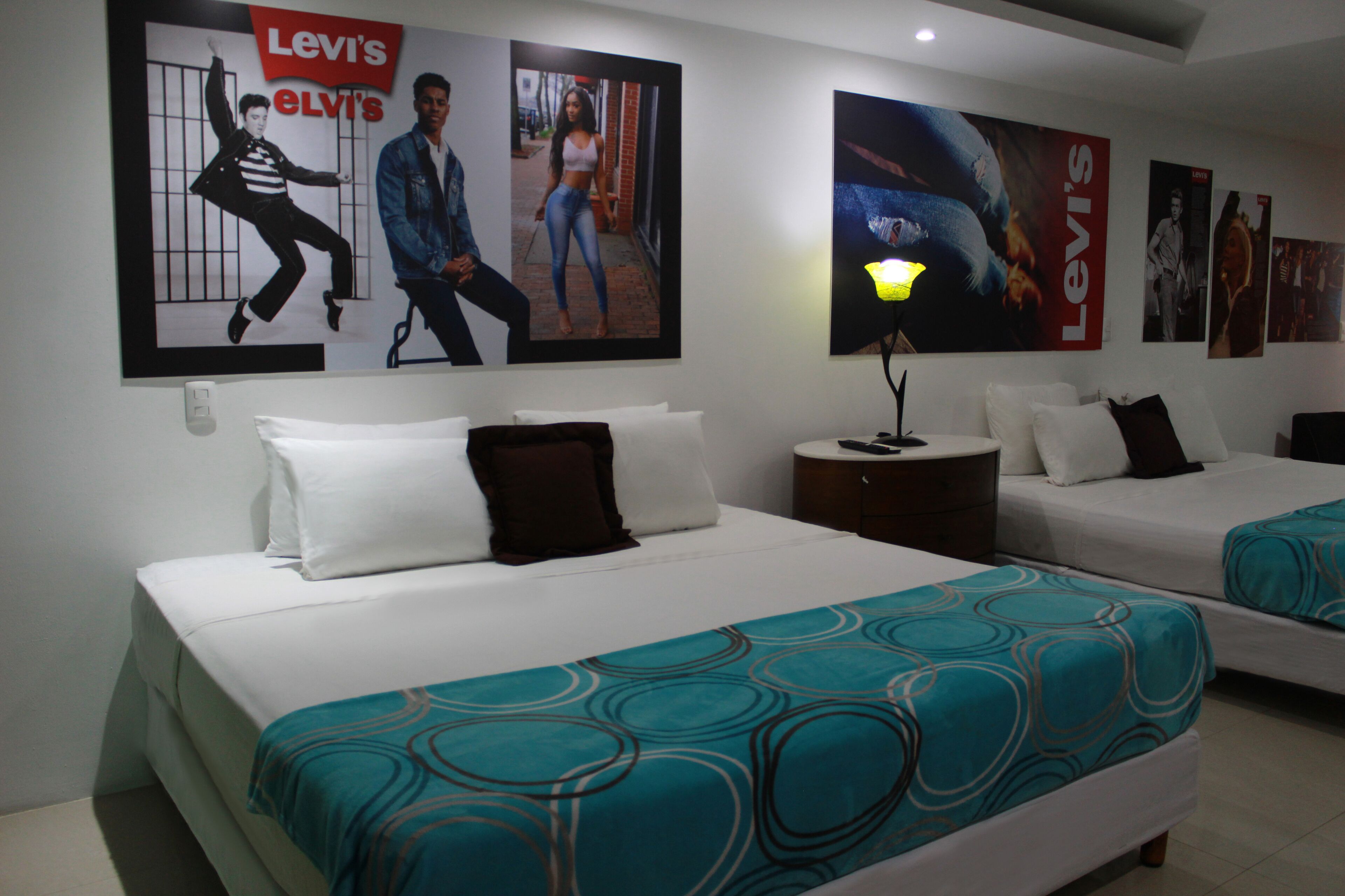 A hotel room with two beds, a nightstand, and posters on the wall.