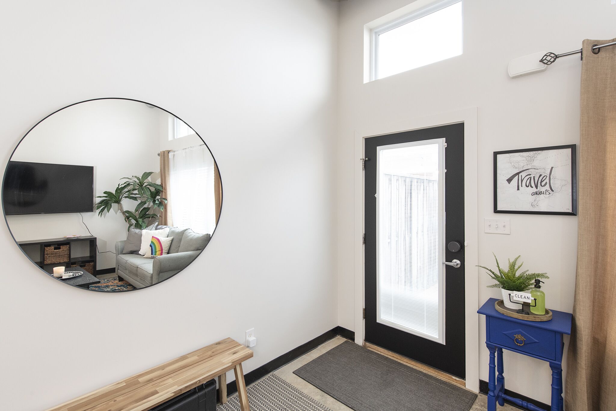 Un salon moderne avec un grand miroir rond, un canapé gris, un petit banc en bois et un téléviseur.