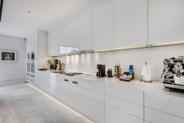 Una cocina moderna con armarios blancos, una campana extractora de acero inoxidable y diversos electrodomésticos.