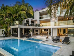 Una casa moderna de varios pisos con piscina, mobiliario exterior y abundante vegetación.