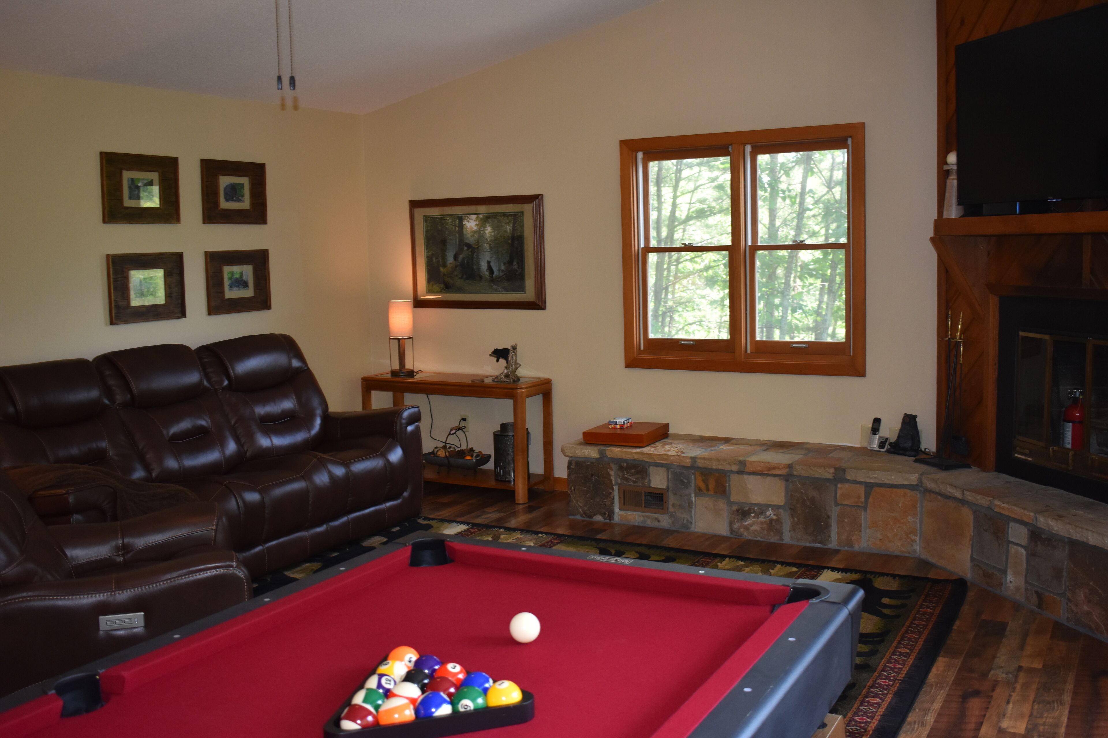Una sala de estar con mesa de billar, sofá de cuero, chimenea de piedra y cuadros en la pared.