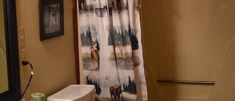 A bathroom with a toilet, sink, and shower curtain with a forest design.