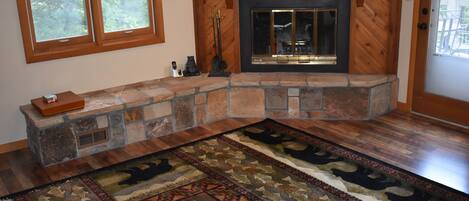 A stone fireplace with a TV above it, a rug with a geometric pattern, and a window with a view of trees.