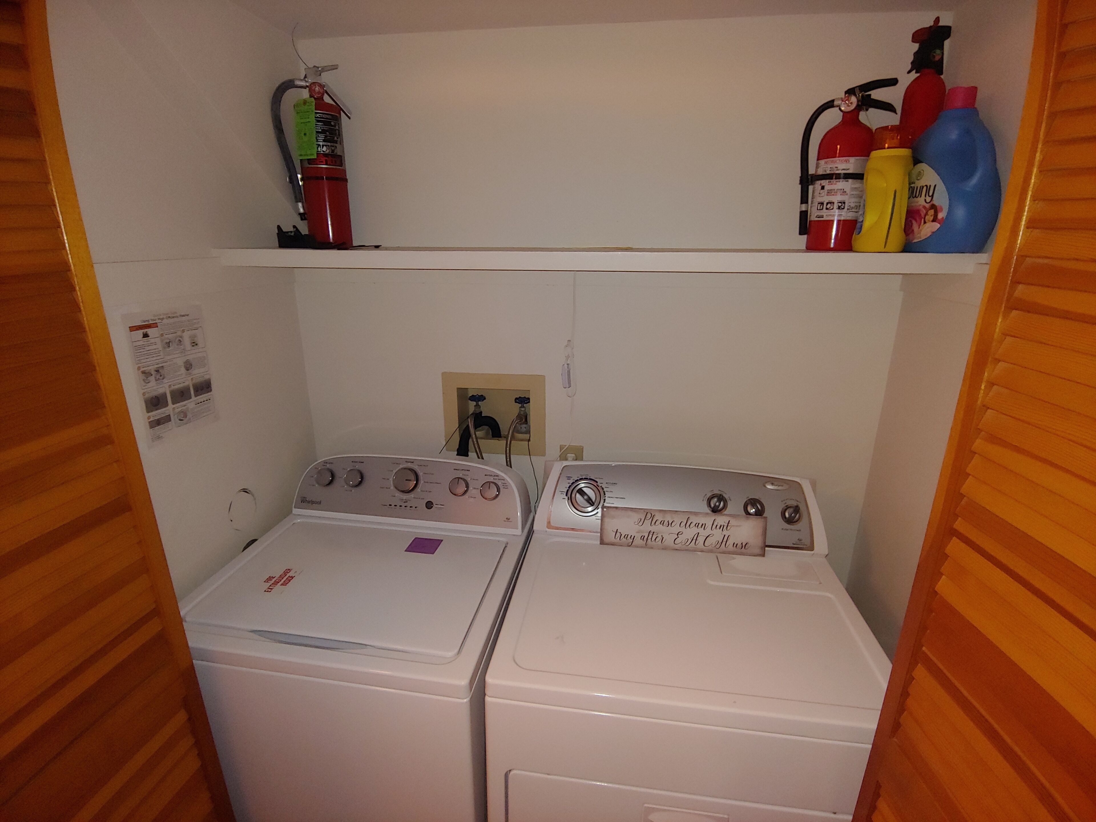 Une buanderie équipée de deux machines à laver, d’un extincteur et de produits de nettoyage rangés sur une étagère.