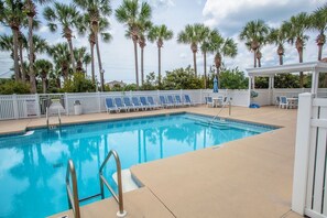 A swimming pool with a white fence, lounge chairs, and palm trees in the background.