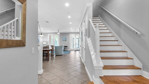 A spacious hallway with a staircase leading to a second floor, a dining area with chairs and a table, and a view of the outside through a door. - Spacious two bedroom, 2 1/2 bath townhome with sleeping loft (Santa Rosa Beach)