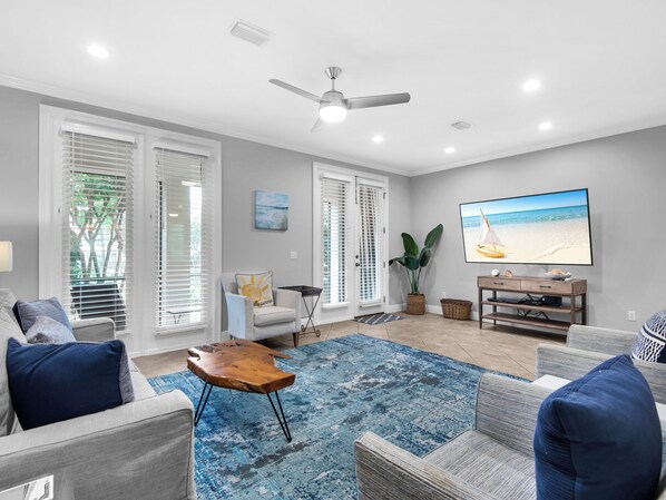 A living room with a large flat-screen TV, a ceiling fan, and a blue patterned rug.