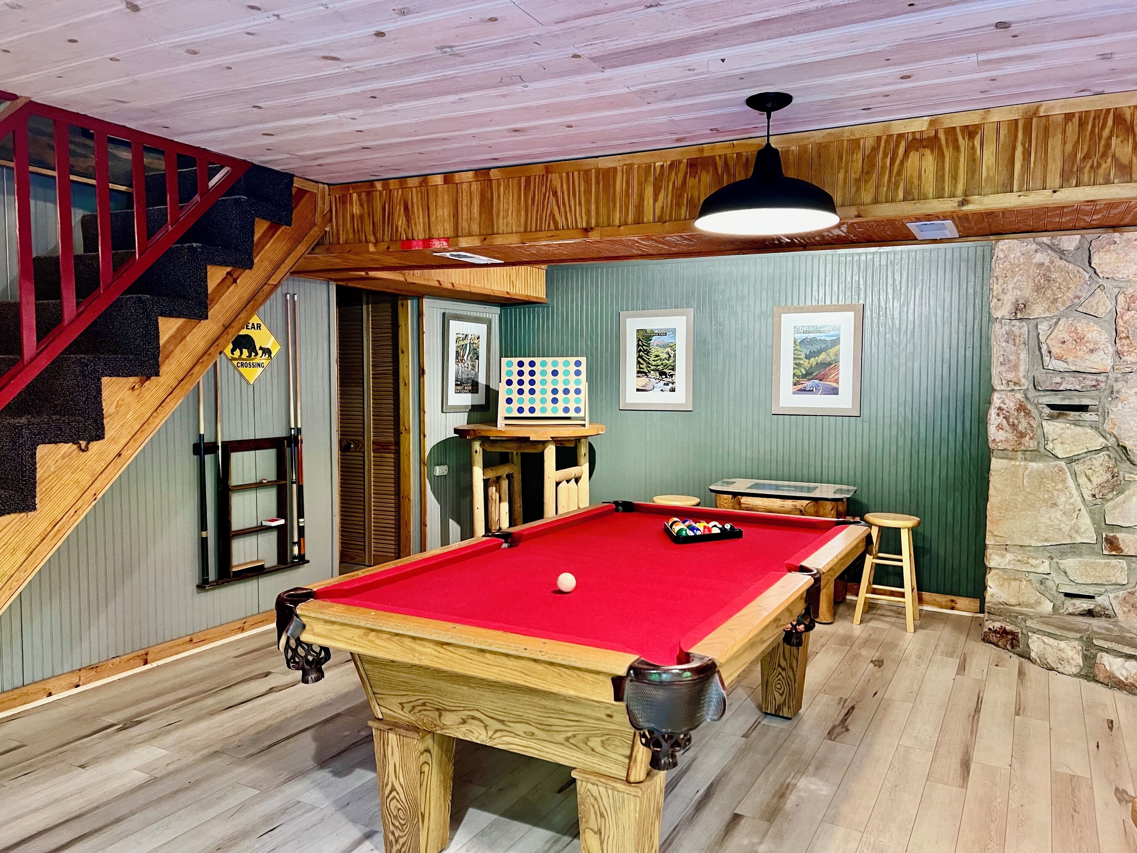 A pool table in a room with wooden floors, a staircase, and a stone wall.