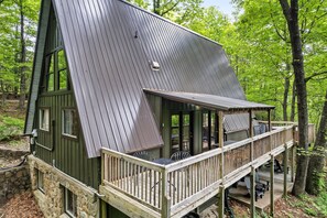 Eine Holzhütte mit geneigtem Dach, einer Terrasse mit Sitzgelegenheiten und einem Steinfundament.