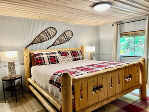 Ein hölzernes Bett mit karierter Bettdecke und einem Kissen mit der Aufschrift 'CABIN sweet cabin'.