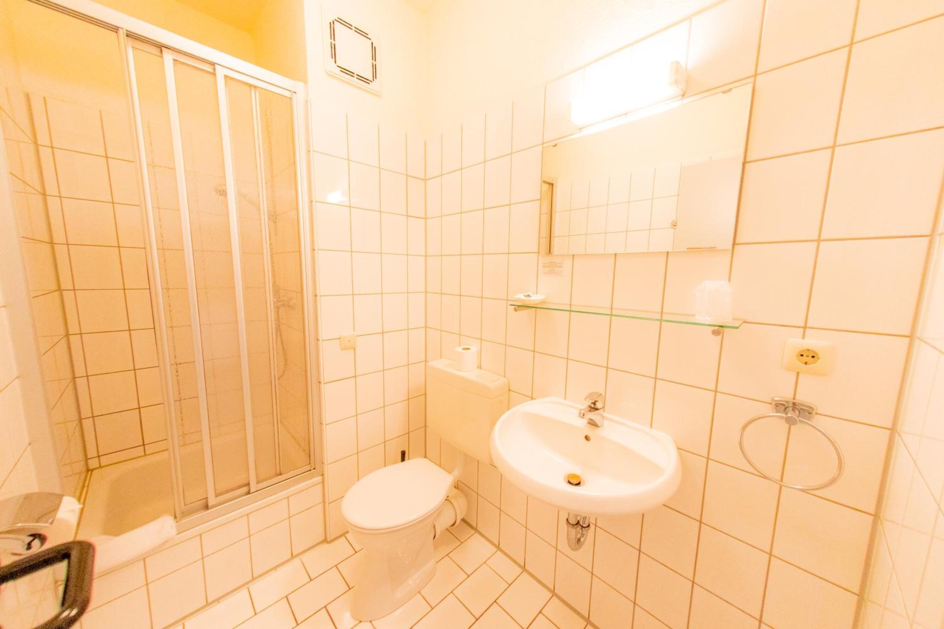 Un baño con ducha, inodoro, lavamanos y espejo.