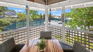 Un espacio al aire libre cubierto con sillas de mimbre y una mesa de madera, con vista a una calle con casas y vegetación.