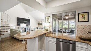 Una cocina moderna con una isla central, muebles blancos y un amplio ventanal con vistas al exterior.