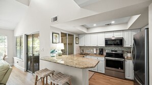 Una cocina moderna con armarios blancos, un refrigerador de acero inoxidable, horno empotrado y una isla grande con taburetes de bar.