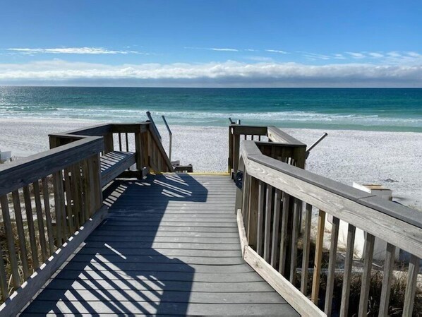 Una pasarela de madera que lleva a una playa, con vista despejada al océano.