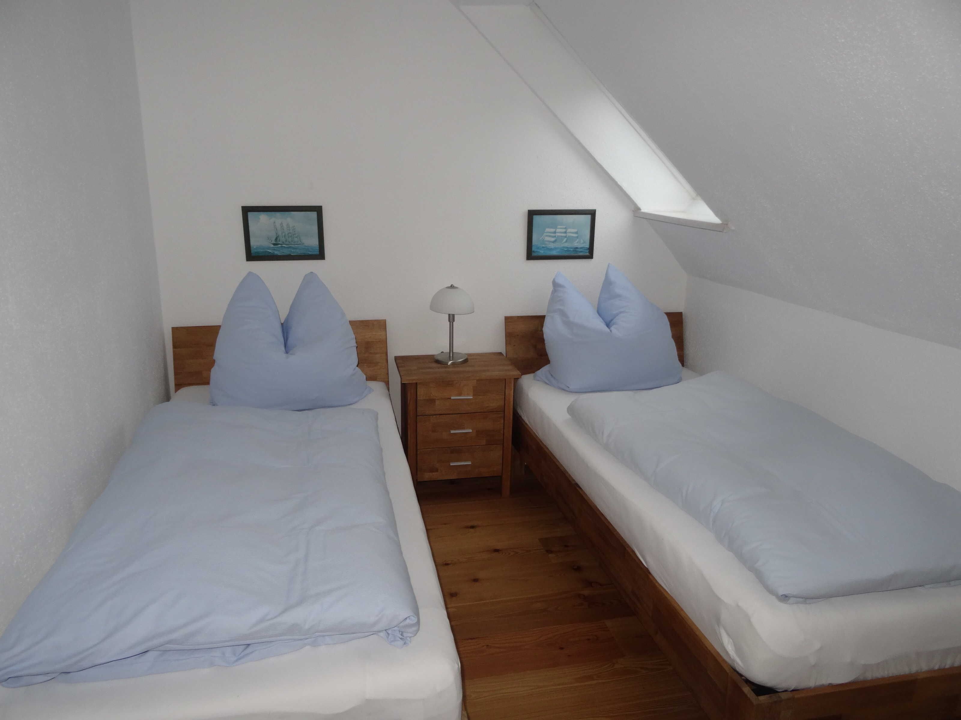 A bedroom with two single beds, a nightstand, a lamp, and two framed pictures on the wall.