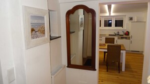A room with a wooden floor, a dining table with chairs, a kitchen area with cabinets and a window, and a framed picture on the wall. - Ferienhaus Urlaub am Meer (Maasholm)