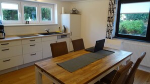 A modern kitchen with a wooden table, chairs, a laptop, and a window with a view of greenery. - Ferienhaus Urlaub am Meer (Maasholm)