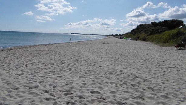 A sandy beach with footprints, a clear sky, and distant shoreline. - Ferienhaus Urlaub am Meer (Maasholm)