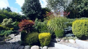 A garden with various shrubs and trees, stone steps, and a clear sky. - Ferienhaus Urlaub am Meer (Maasholm)