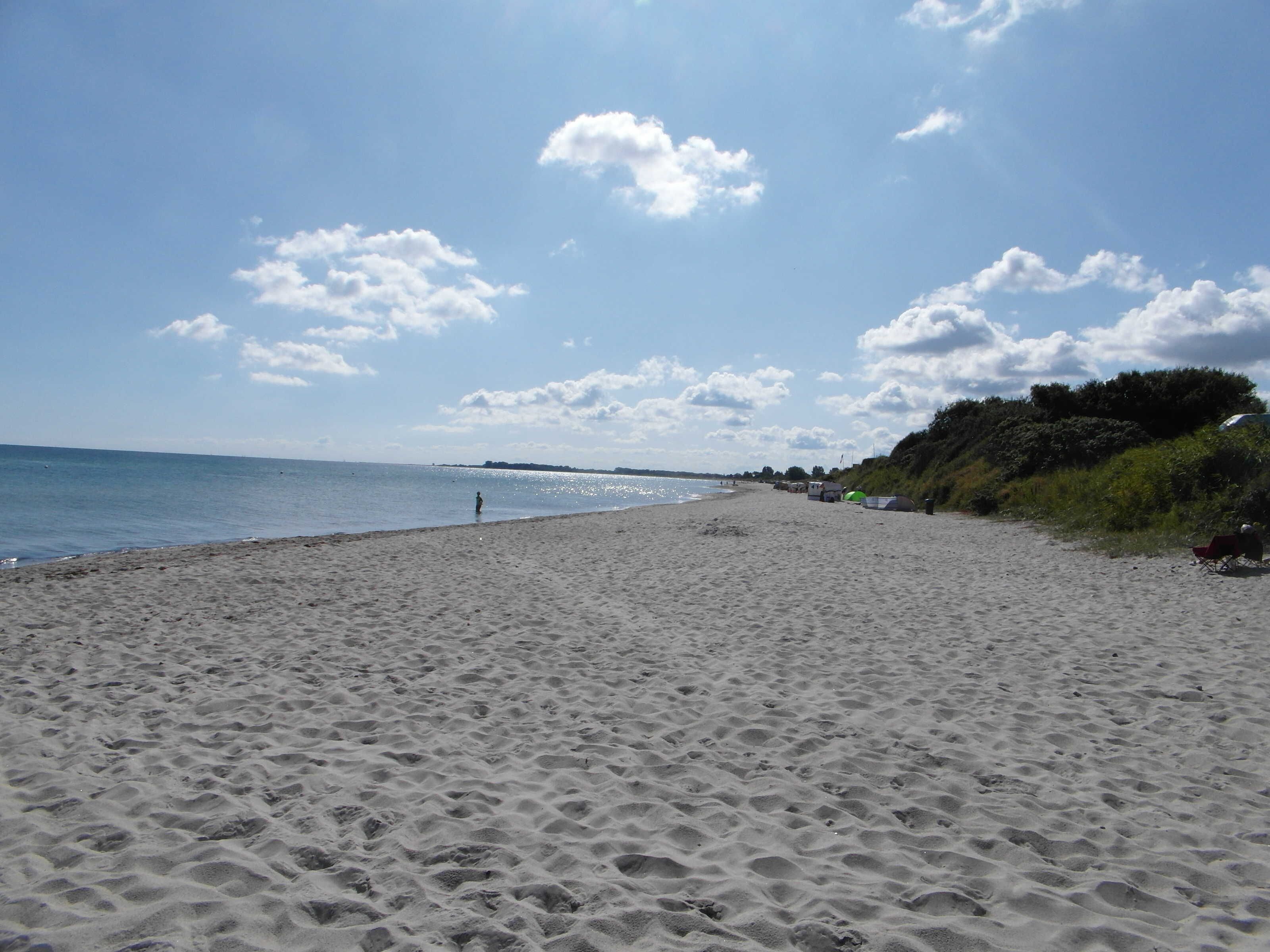 Une plage de sable parsemée d’empreintes, un ciel dégagé et une côte lointaine.