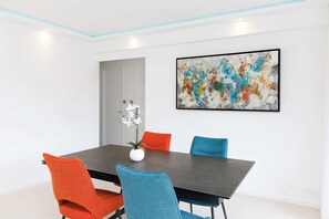 Un comedor moderno con una mesa oscura, sillas coloridas y un jarrón blanco con flores.