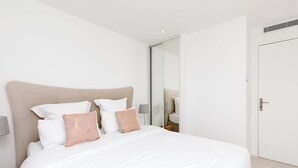 A neatly made bed with white bedding and two decorative pillows, a bedside table with a lamp, and a door with a handle.