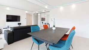 A modern living room with a black sofa, blue chairs, a grey table, and a flat-screen TV mounted on the wall.