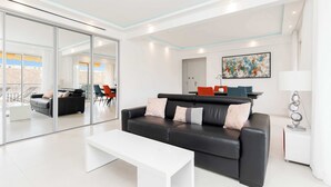 A modern living room with a black sofa, white coffee table, and glass sliding doors leading to an outdoor area.