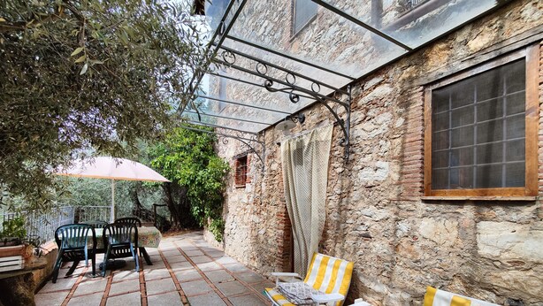 A stone-walled outdoor patio with a table and chairs, a covered seating area, and a window. - Detached house in nature suitable for families (2 double bedrooms) and dogs (Camaiore)