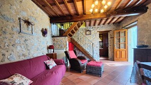 A rustic interior with a wooden ceiling, stone walls, a red sofa, wicker furniture, and a staircase leading to an upper level. - Detached house in nature suitable for families (2 double bedrooms) and dogs (Camaiore)