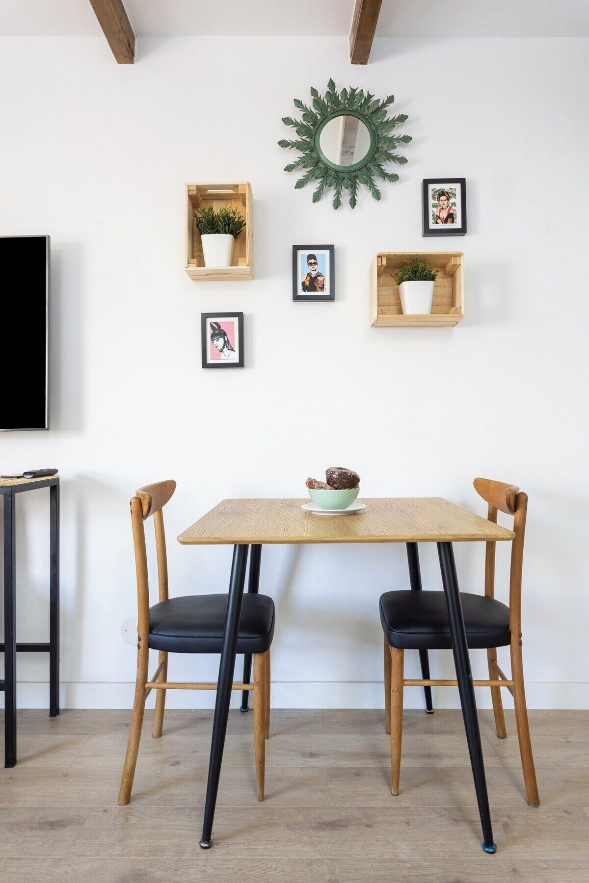 En matplats med ett träbord, två stolar, en skål med mat och väggdekorationer, inklusive inramade bilder och en spegel.