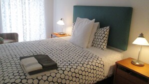 A neatly made bed with a patterned bedspread, a bedside lamp, and a small wooden nightstand with a lamp.
