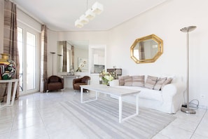 A modern living room with a white sofa, a coffee table, a dining table with chairs, a large mirror, and a floor lamp. - Croisette Boulevard deluxe apartment (Cannes)