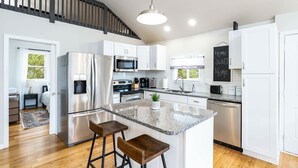 A modern kitchen with stainless steel appliances, white cabinetry, and a granite countertop. - Loft cabin w/hot tub, deck & fire pit (Hedgesville)