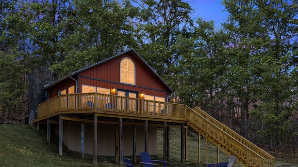 A cabin with a wooden deck, a staircase, and two Adirondack chairs by a fire pit. - Loft cabin w/hot tub, deck & fire pit (Hedgesville)