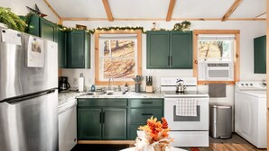 A modern kitchen with green cabinets, stainless steel appliances, and a window with a view of autumn leaves. - Cozy Cabin w Lake, Hot Tub, Huge Deck & Fire Pit (Mathias)